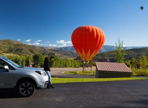 A woman standing outside her car and watching hot air balloons nearby