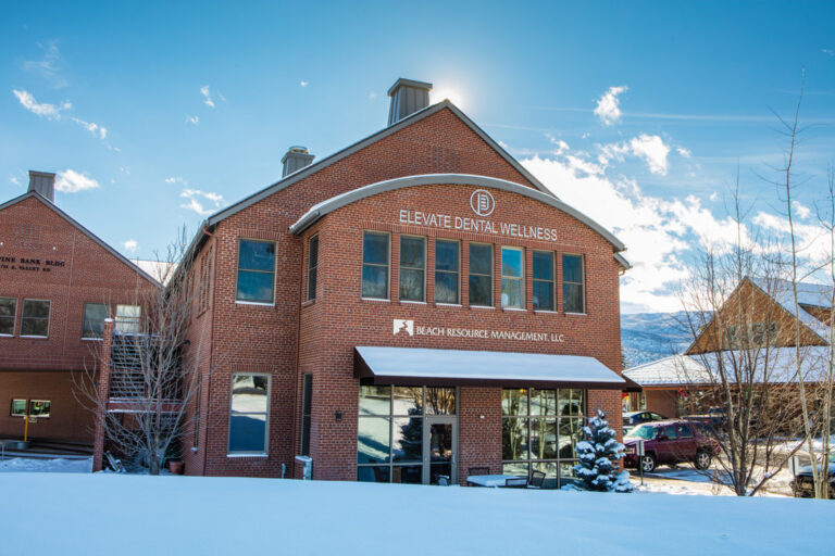 Brick office building in snowy mountain setting with signage for Elevate Dental Wellness and Beach Resource Management.
