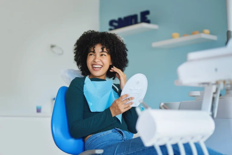A smiling patient admiring their teeth in a handheld mirror after dental treatment in a modern clinic.
